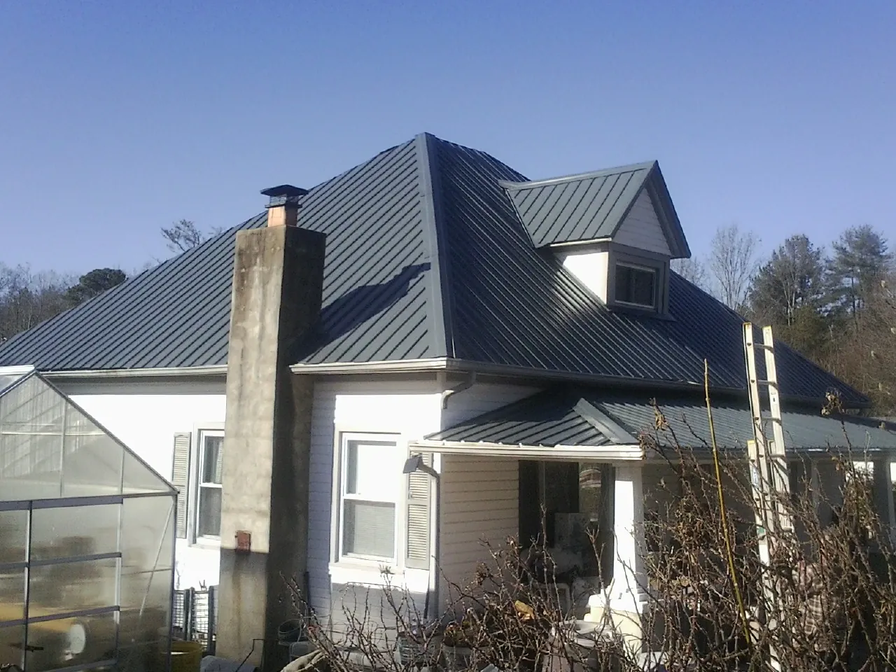 Dark blue standing seam metal roof on a white farmhouse with dormer — Slate & Tile Roof Repair by Roofing Brothers in Courtland
